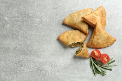 Photo of Fresh delicious crispy samosas, rosemary and tomatoes on grey table, flat lay. Space for text