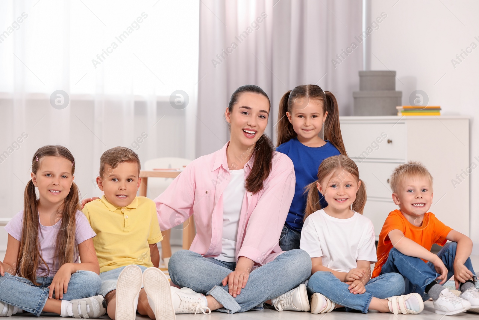 Photo of Happy nursery teacher and group of cute little children on floor in kindergarten. Playtime activities