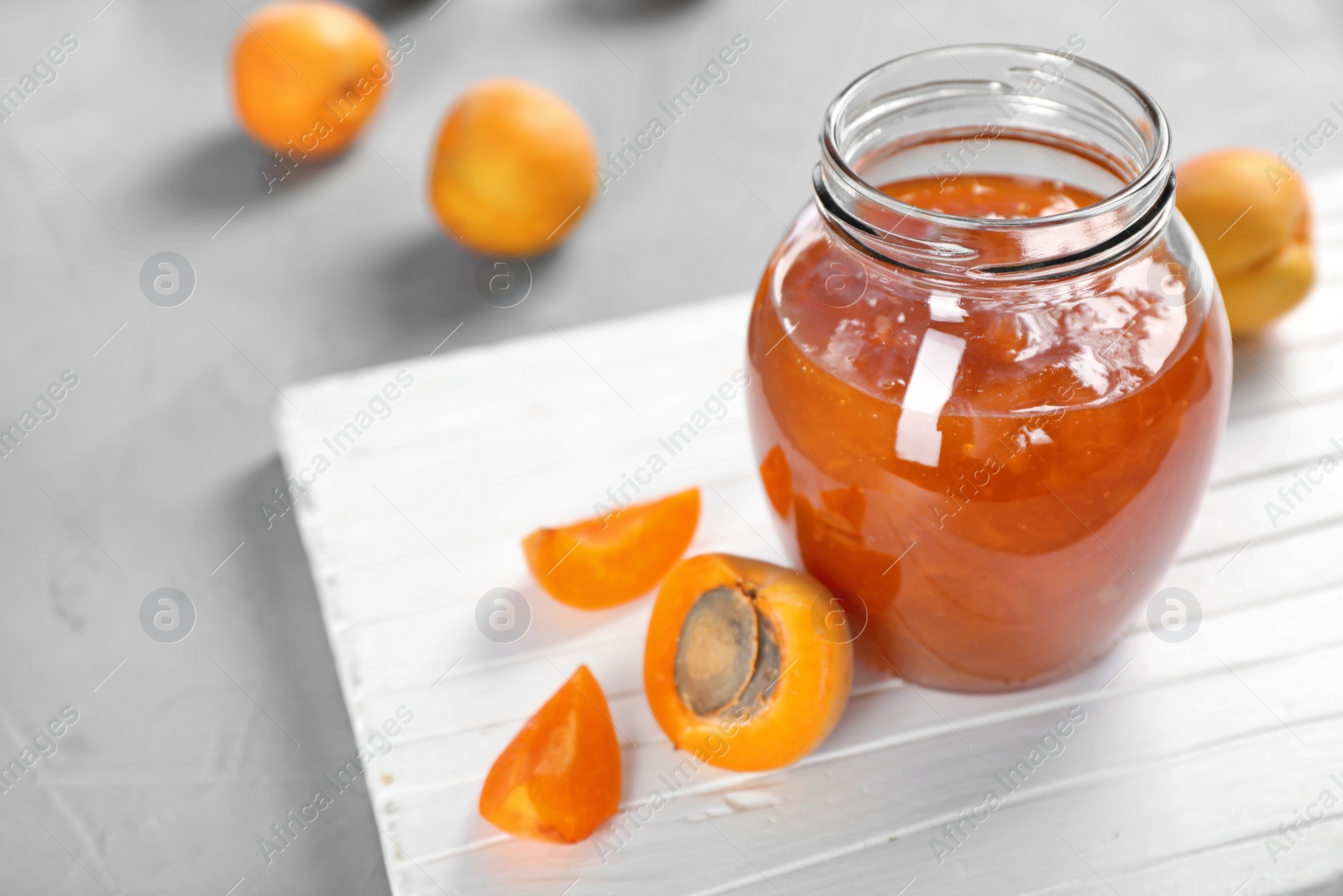 Photo of Jar with tasty apricot jam on wooden board