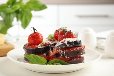 Photo of Baked eggplant with tomatoes, cheese and basil served on kitchen table, closeup