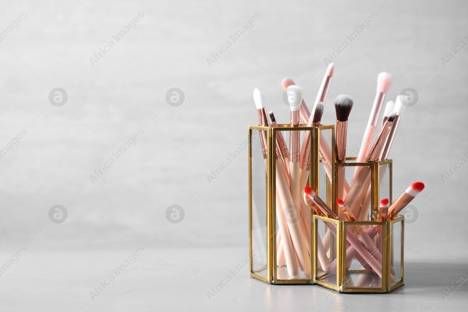 Photo of Make up brushes in holders on white table. Space for text