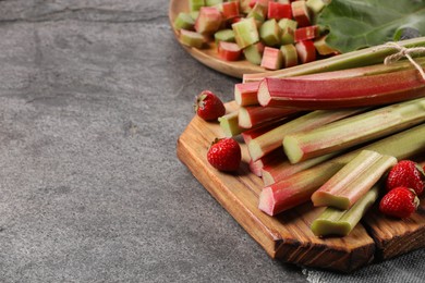 Photo of Fresh ripe rhubarb stalks and strawberries on grey table, closeup. Space for text