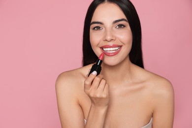 Photo of Beautiful young woman applying glossy lipstick on pink background. Space for text