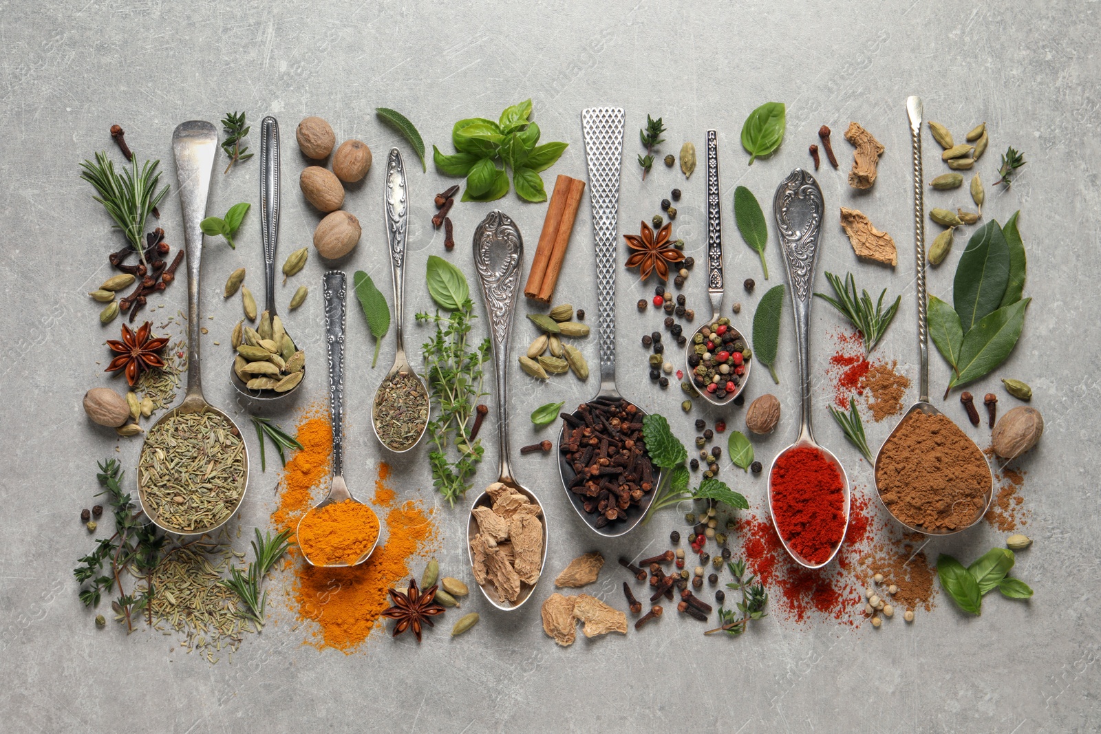 Photo of Different herbs and spices with spoons on grey table, flat lay