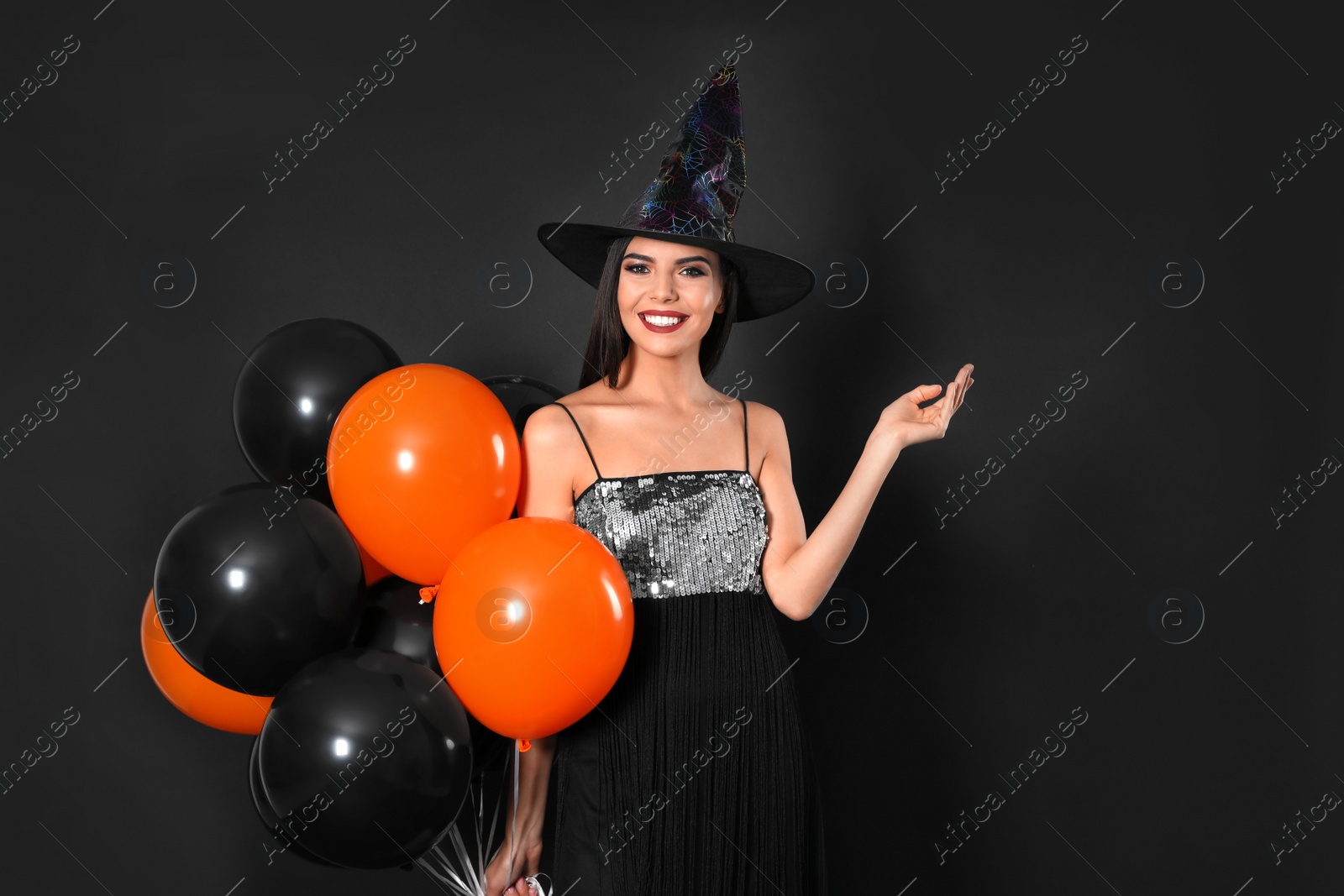 Photo of Beautiful woman wearing witch costume with balloons for Halloween party on black background