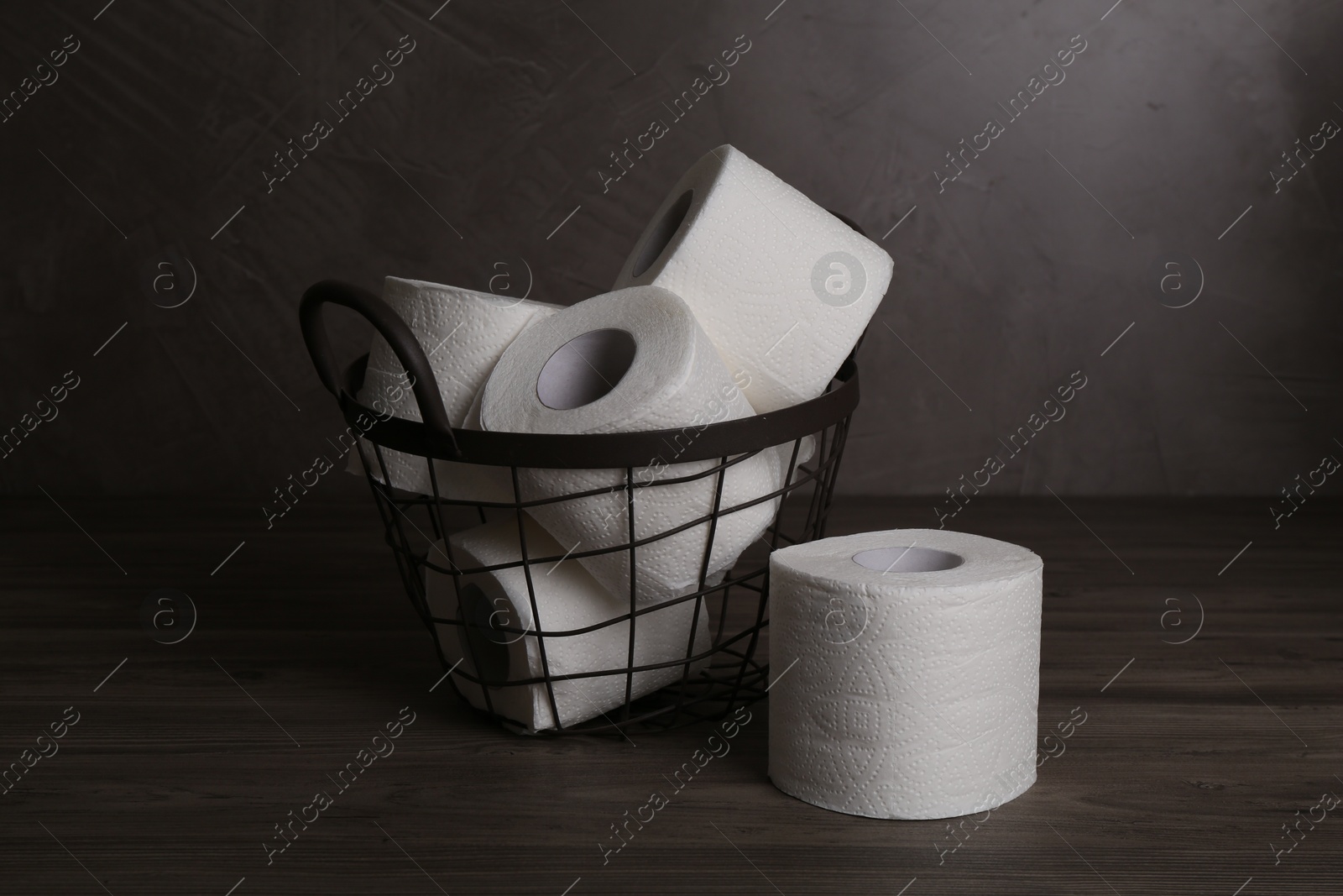 Photo of Soft toilet paper rolls in metal basket on wooden table