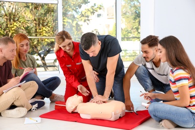 Photo of Group of people with instructor practicing CPR on mannequin at first aid class indoors