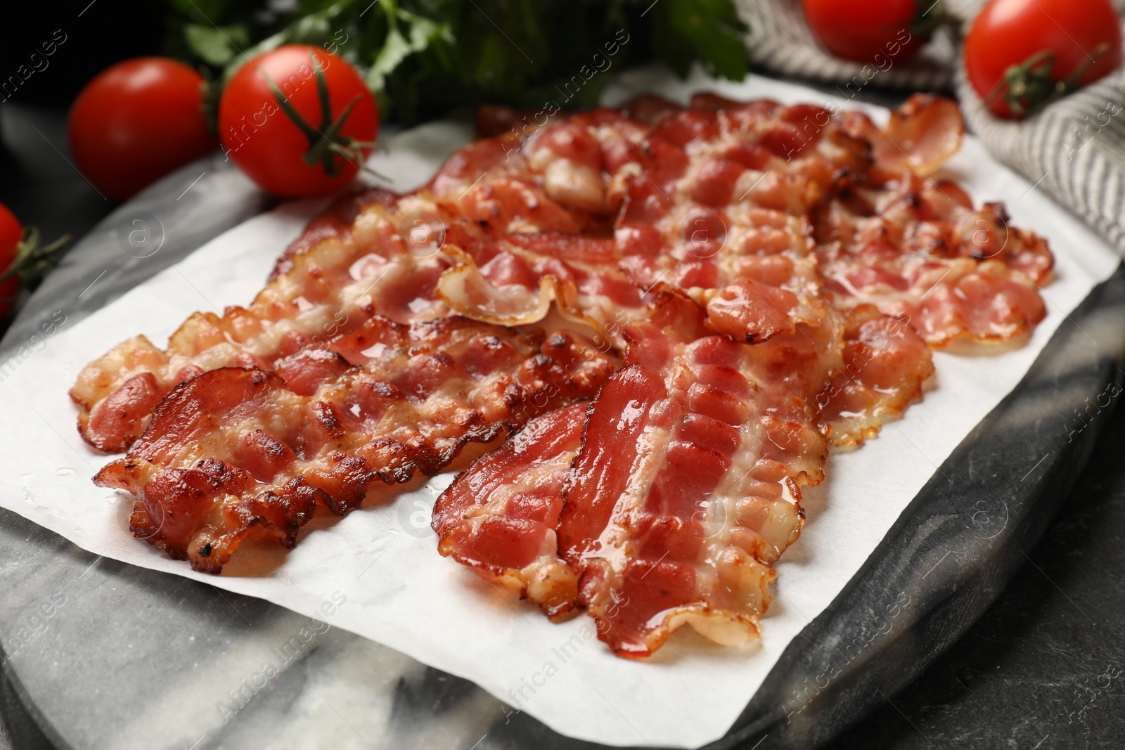 Photo of Fried bacon slices and tomatoes on dark table, closeup