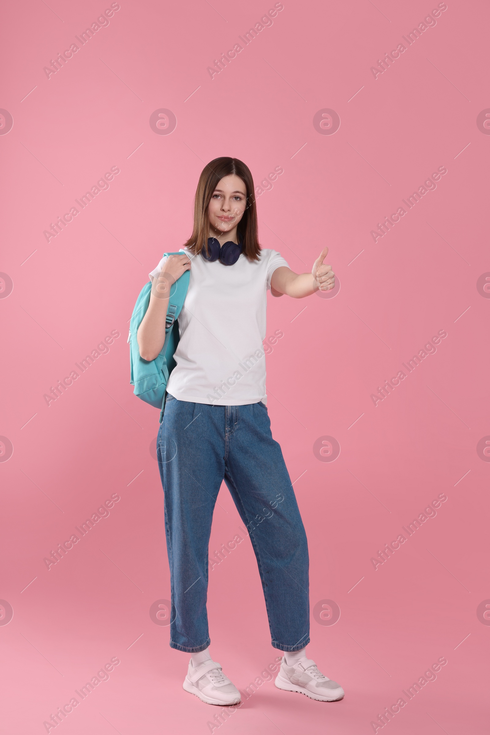 Photo of Cute teenage girl showing thumb up on pink background