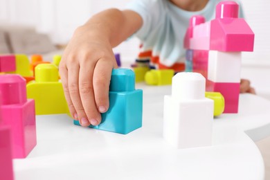 Photo of Little child playing with colorful building blocks at table indoors, closeup