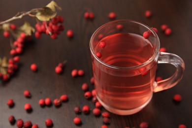 Cup with hawthorn tea and berries on wooden table, closeup. Space for text