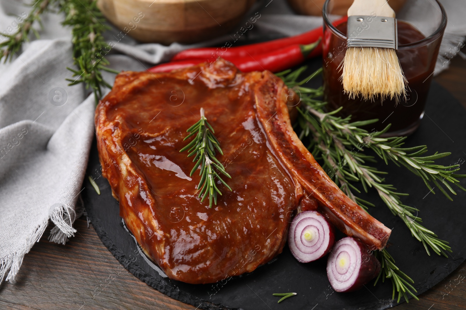 Photo of Tasty marinated meat, rosemary and onion on wooden table, closeup