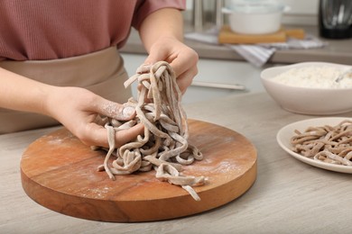 Photo of Woman making soba (buckwheat noodles) at wooden table in kitchen, closeup