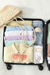 Photo of Open suitcase packed for trip and straw bag on white blanket, flat lay