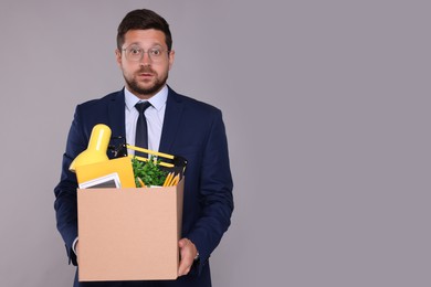 Photo of Surprised unemployed man with box of personal office belongings on grey background. Space for text