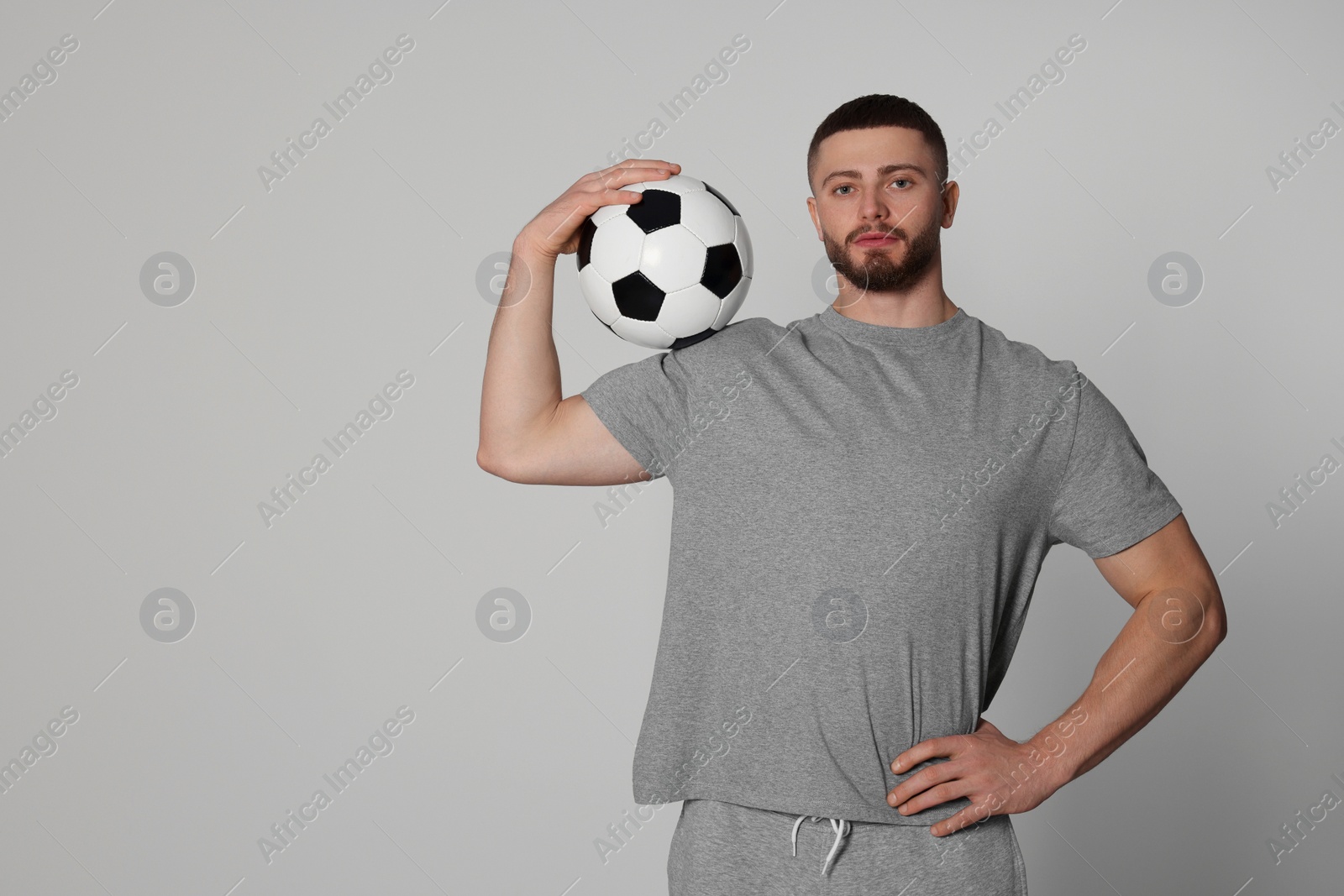 Photo of Athletic young man with soccer ball on light grey background. Space for text