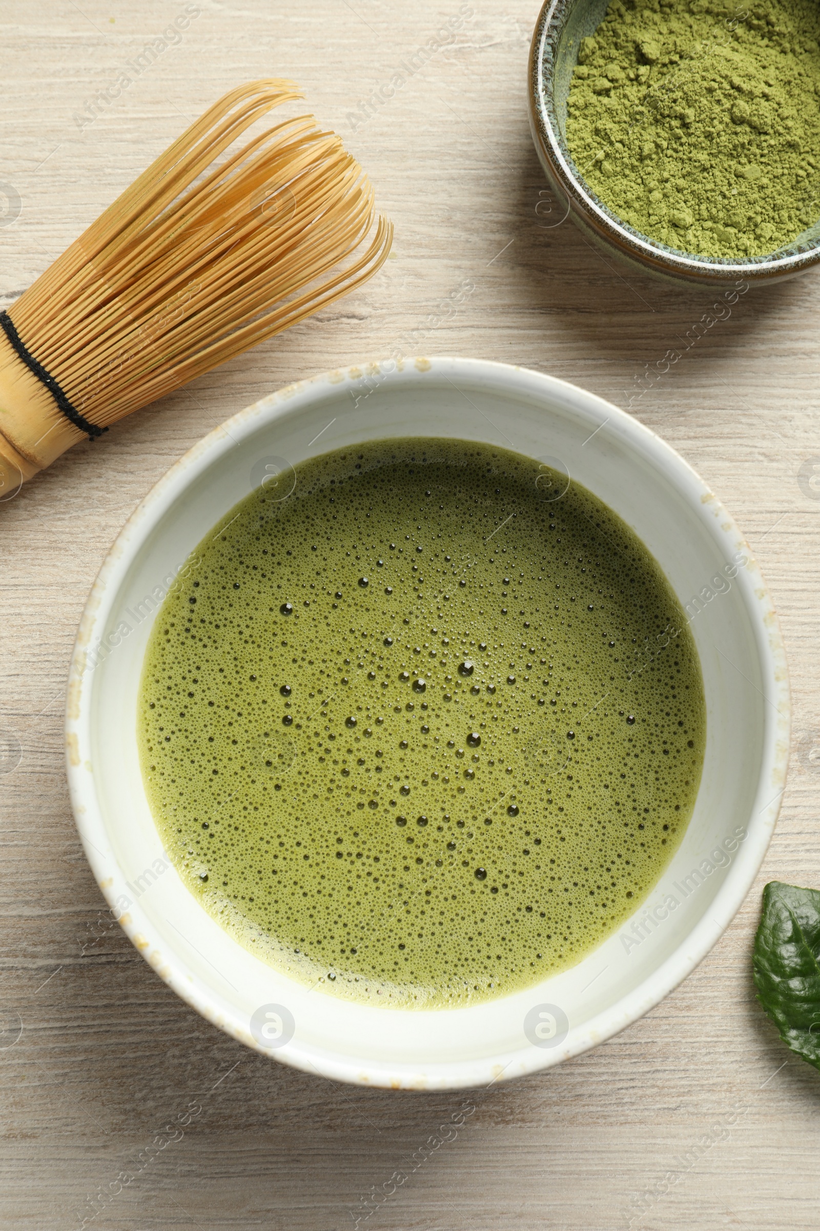 Photo of Cup of fresh matcha tea, green powder and bamboo whisk on white wooden table, flat lay