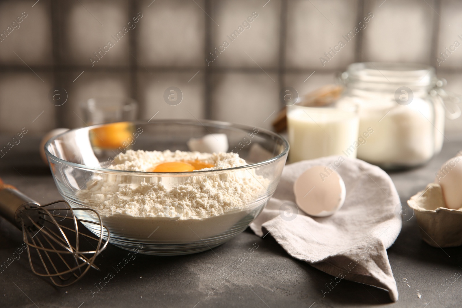 Photo of Making dough. Flour with egg yolk in bowl and whisk on grey textured table, closeup
