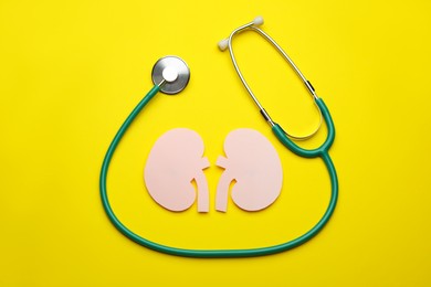 Paper cutout of kidneys and stethoscope on yellow background, flat lay