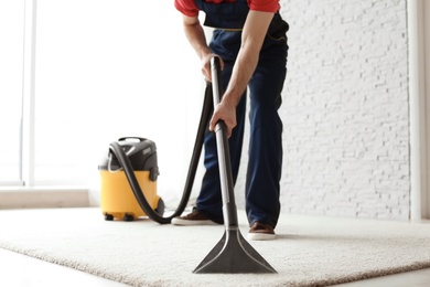 Photo of Male worker cleaning carpet with vacuum indoors