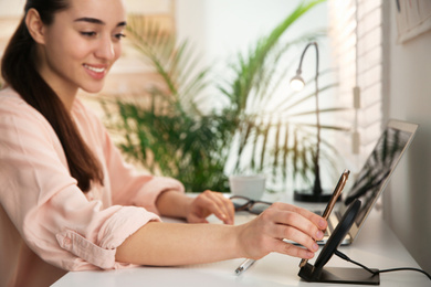 Woman putting mobile phone onto wireless charger at white table indoors. Modern workplace accessory