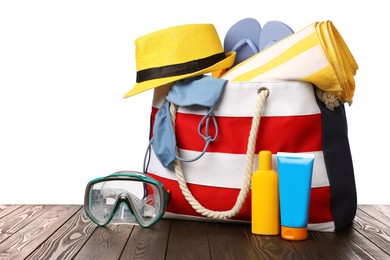 Photo of Stylish bag with beach accessories on wooden table against white background