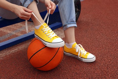 Photo of Woman tying shoelace of yellow classic old school sneaker on basketball ball at outdoor court, closeup