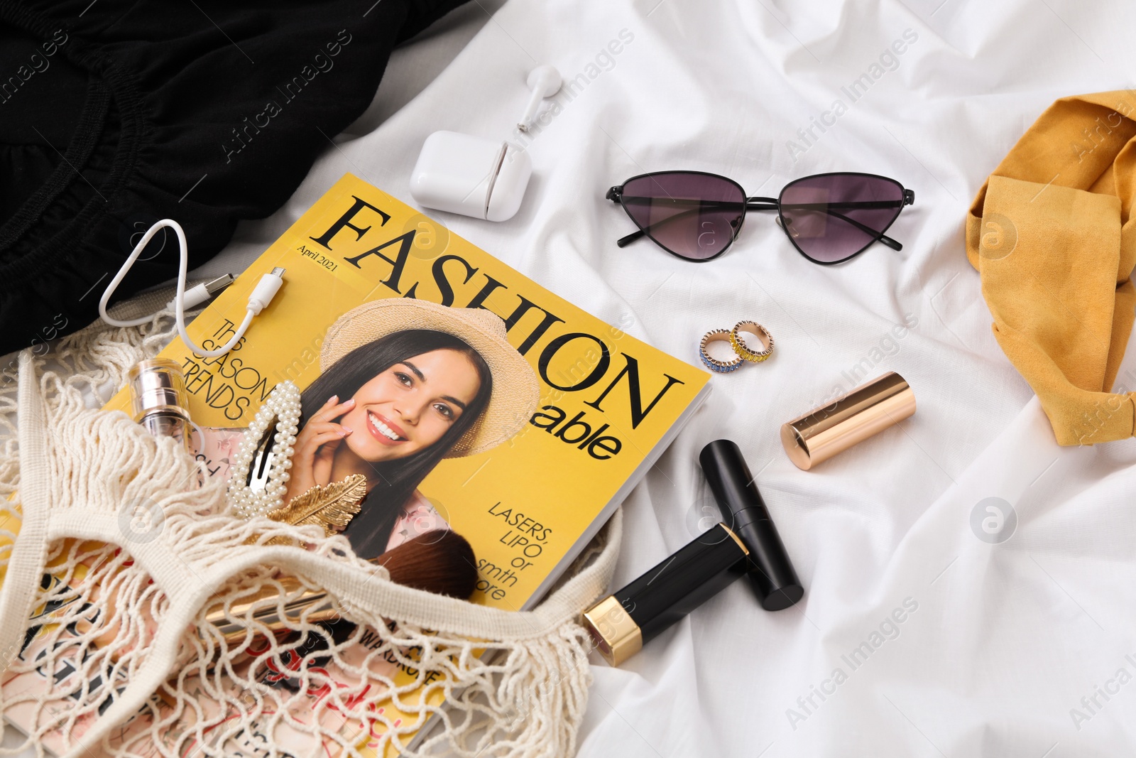 Photo of Bag with fashion magazine, earphones and accessories on white fabric