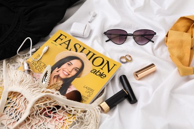 Photo of Bag with fashion magazine, earphones and accessories on white fabric