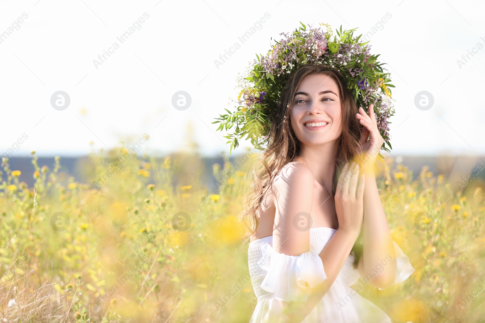 Photo of Young woman wearing wreath made of beautiful flowers in field on sunny day