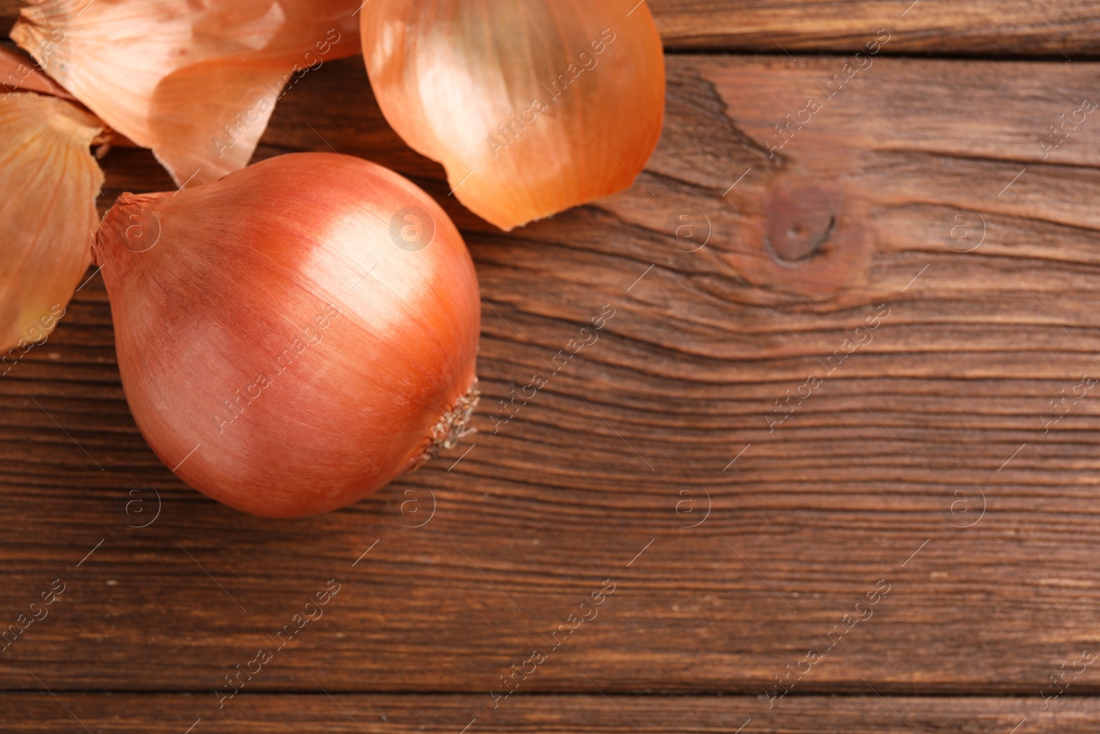 Photo of Fresh ripe onion and husk on wooden table, flat lay. Space for text