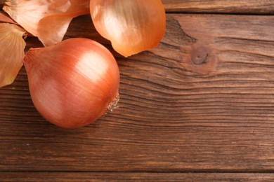 Photo of Fresh ripe onion and husk on wooden table, flat lay. Space for text