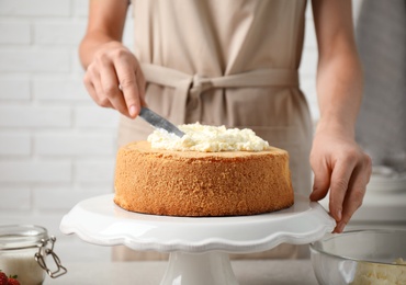 Photo of Woman decorating delicious cake with fresh cream at table indoors, closeup. Homemade pastry