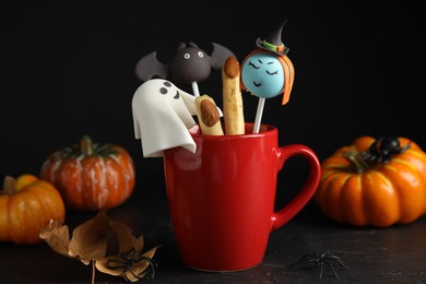 Different cake pops in cup decorated as monsters on black table. Halloween treat