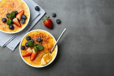 Photo of Delicious creme brulee with berries and mint in bowls on grey table, flat lay. Space for text