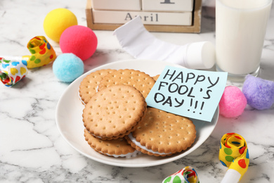 Photo of Cookies with toothpaste and HAPPY FOOL'S DAY note on white marble table. April holiday