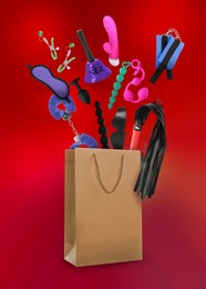 DIfferent sex toys and accessories falling into paper shopping bag on red background