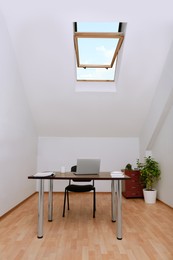 Photo of Stylish workplace with laptop and documents in attic room. Interior design