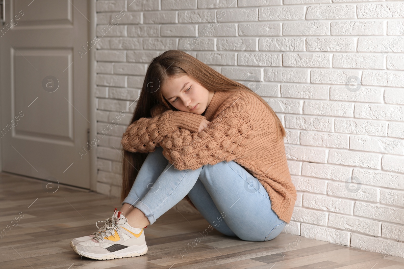 Photo of Upset teenage girl sitting alone on floor near wall