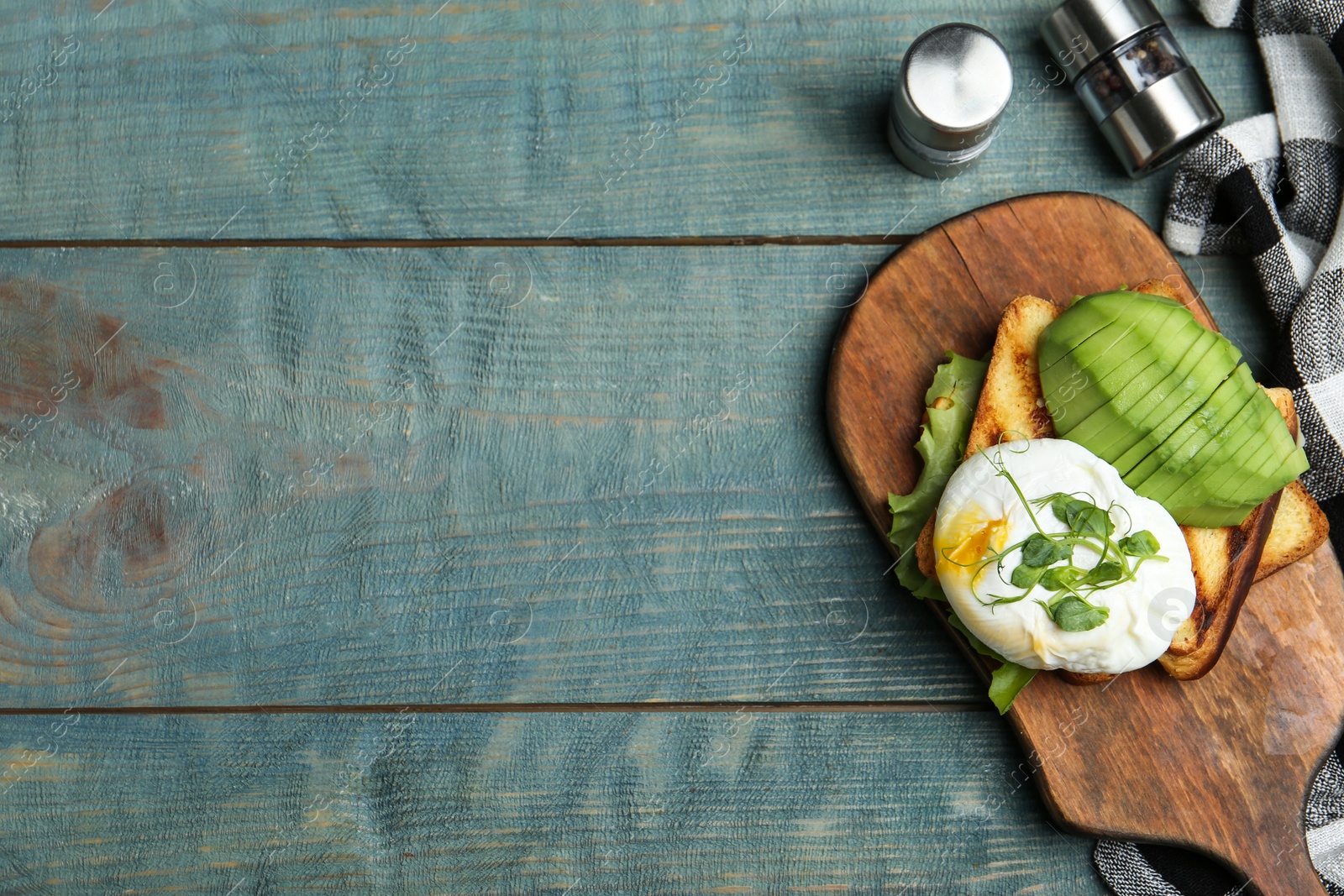 Photo of Delicious poached egg with toasted bread and avocado served on blue wooden table, flat lay. Space for text