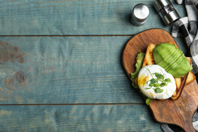 Delicious poached egg with toasted bread and avocado served on blue wooden table, flat lay. Space for text