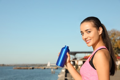 Young sporty woman with water bottle outdoors on sunny day. Space for text