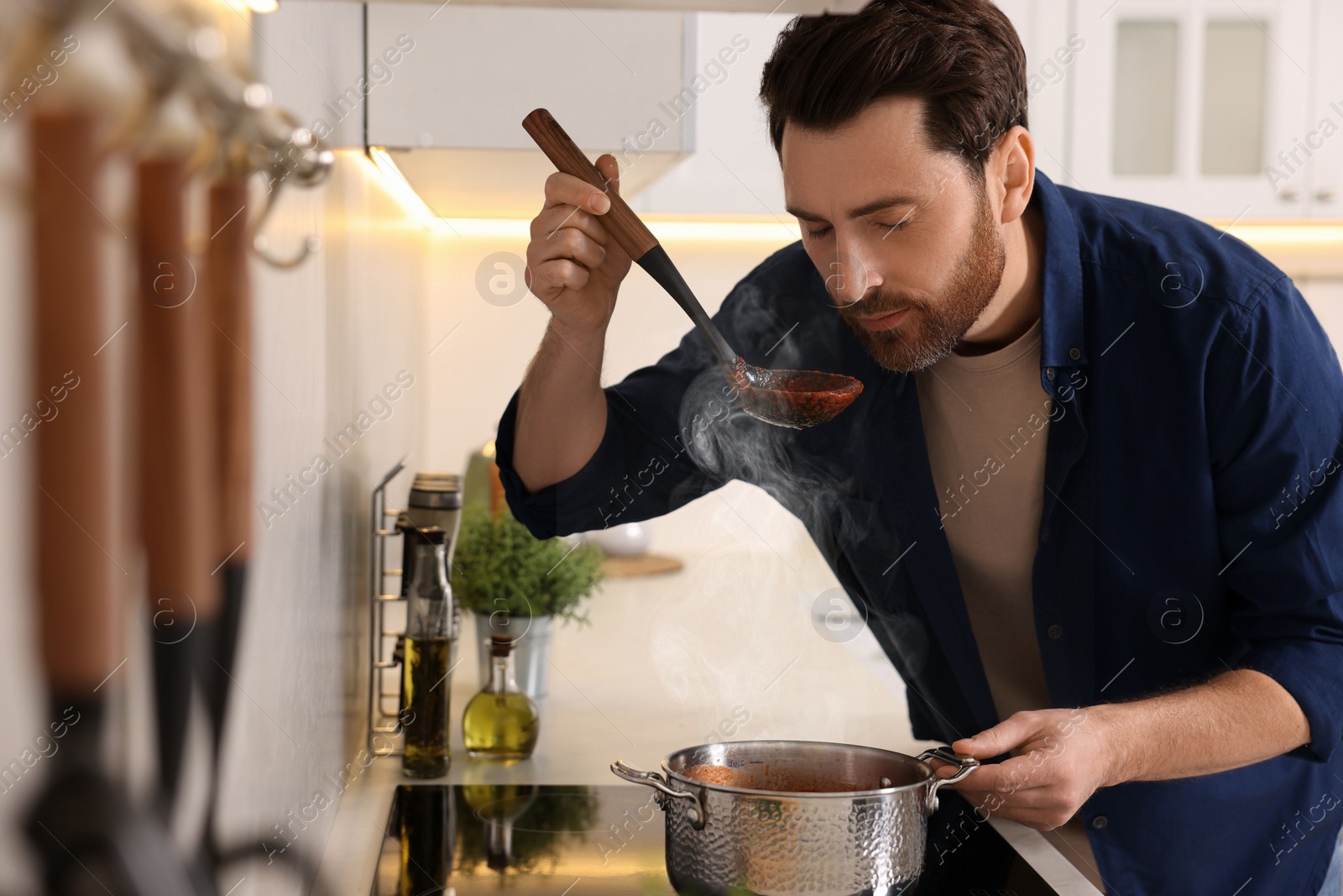 Photo of Man tasting delicious tomato soup in kitchen