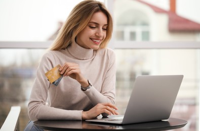 Photo of Woman with credit cards using laptop for online shopping indoors