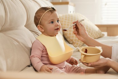 Photo of Mother feeding her little baby at home. Kid wearing silicone bib