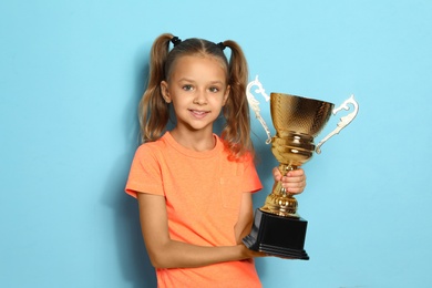 Happy girl with golden winning cup on blue background