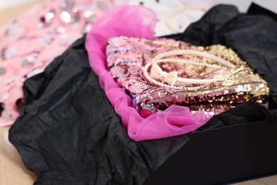 Headbands and stylish pink carnival costume with sequins in black box on wooden table, closeup