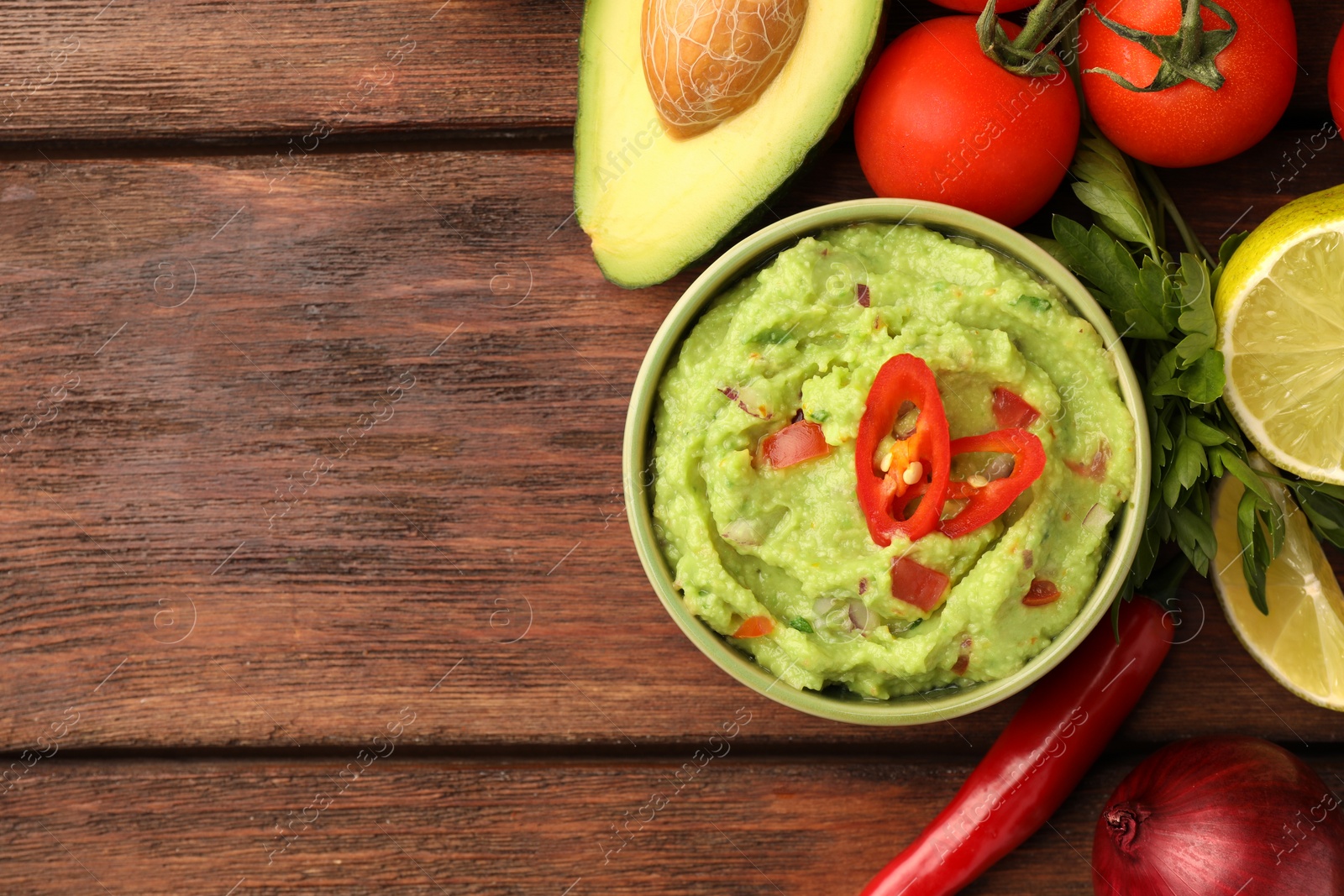 Photo of Bowl of delicious guacamole and ingredients on wooden table, flat lay. Space for text
