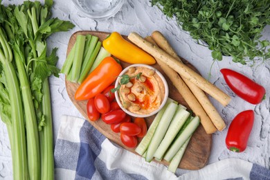 Board with delicious hummus, grissini sticks and fresh vegetables on light grey textured table, flat lay