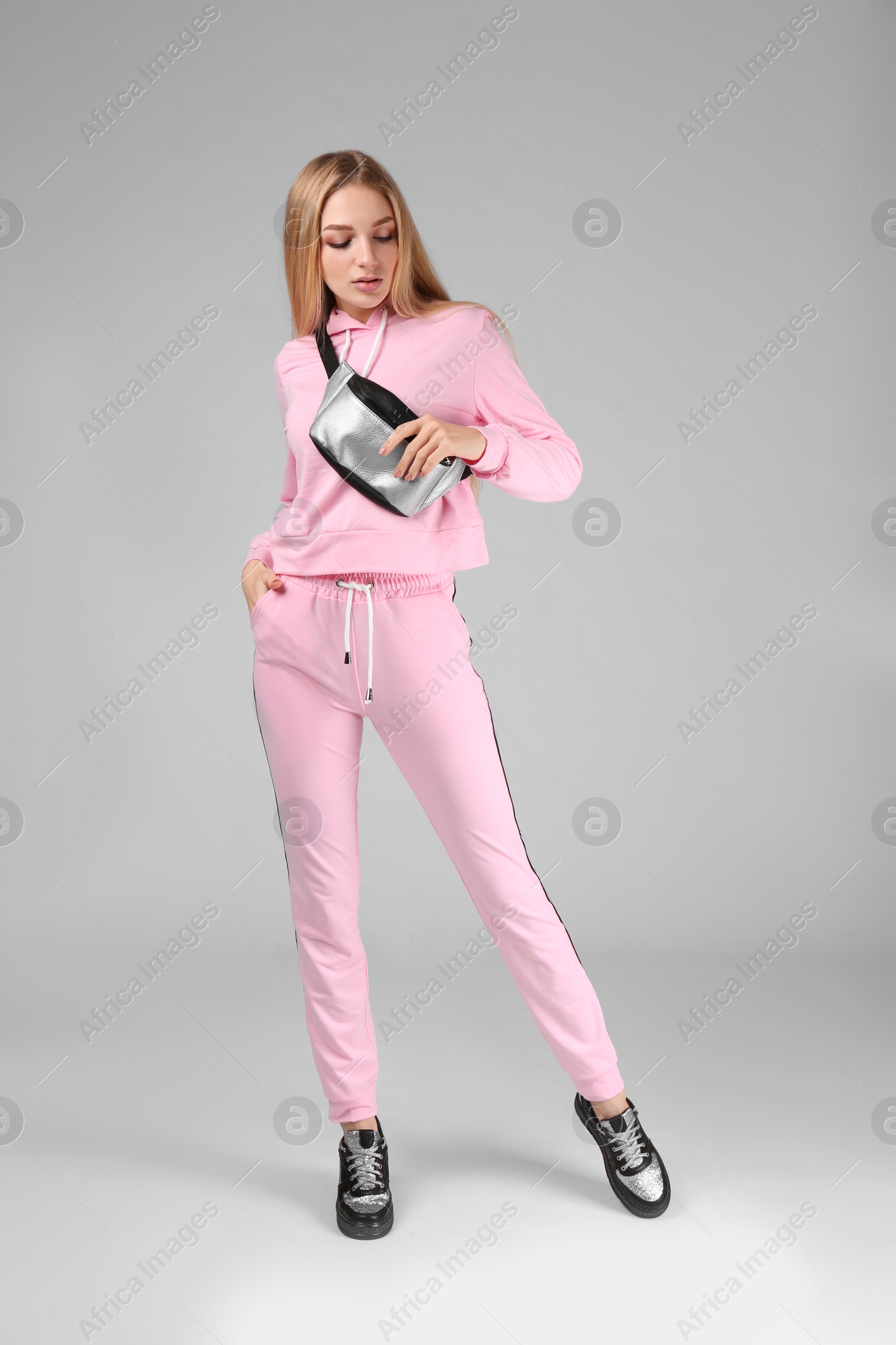 Photo of Young stylish woman in trendy sport shoes with bum bag on light background